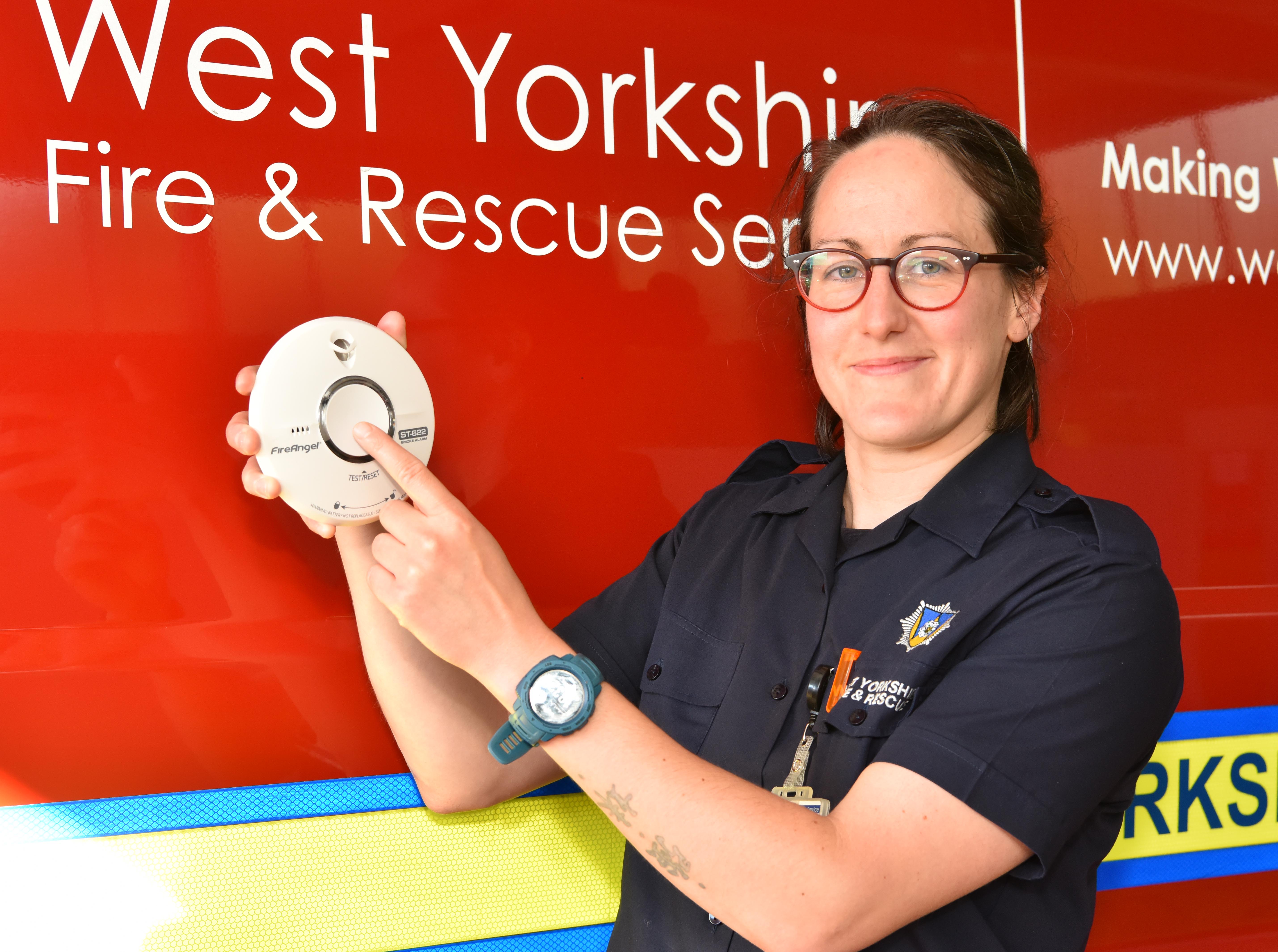 Firefighter holding smoke alarm and pointing to it.