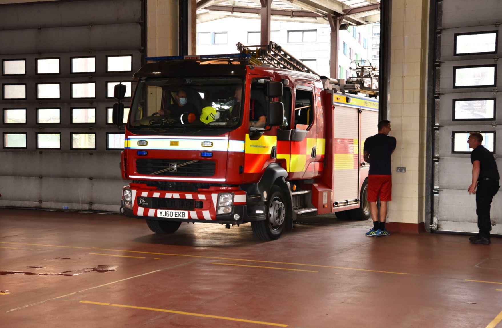 Fire engine parked in fire station with firefighters opening door. 