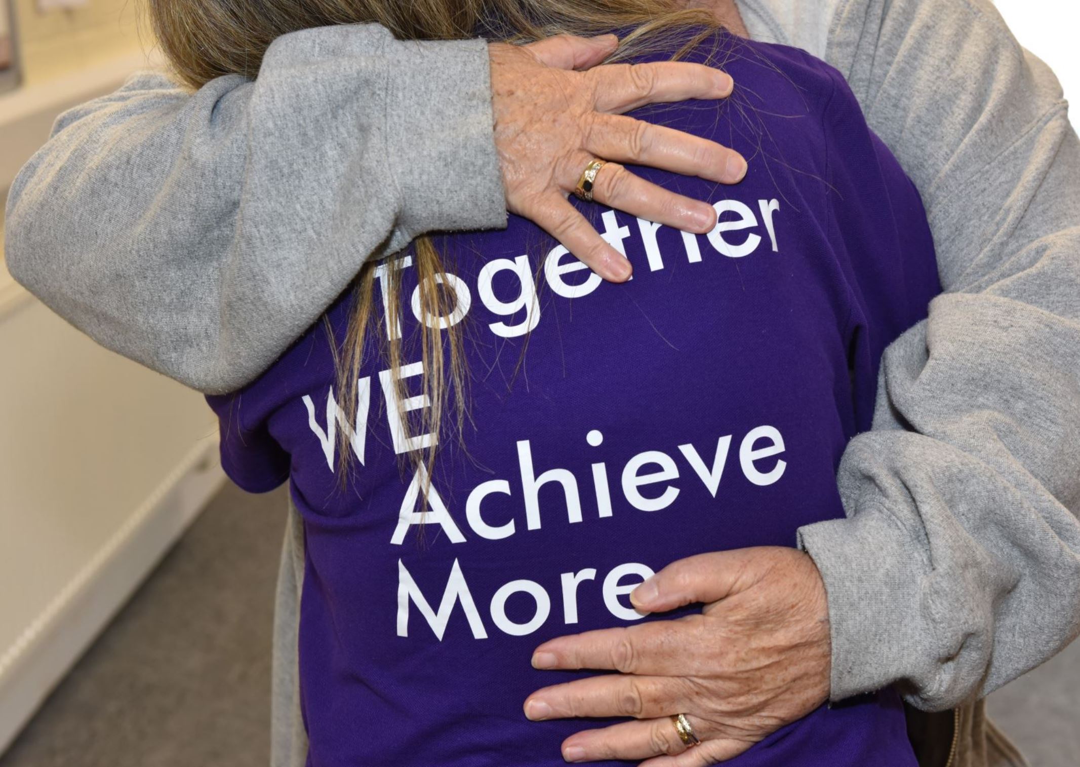 Two people hugging. The words "Together we achieve more" written on the back of a t shirt. 