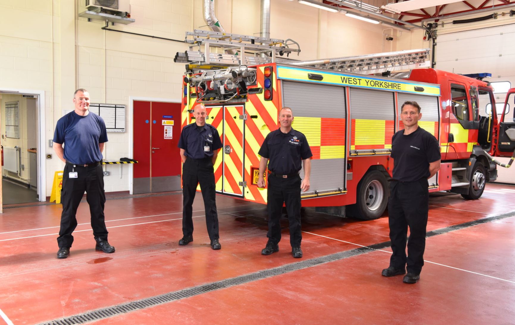 Firefighters stood in front of fire engines, looking at the camera. 