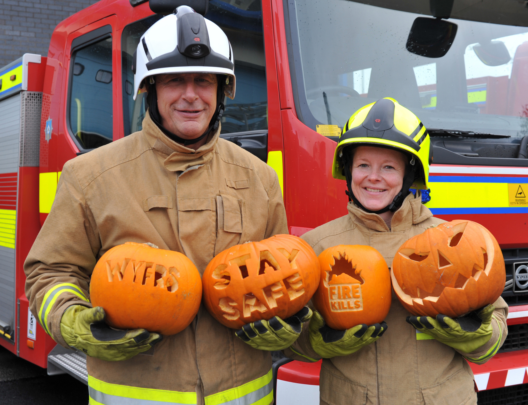 Firefighters holding carved pumpkins in front of fire engine