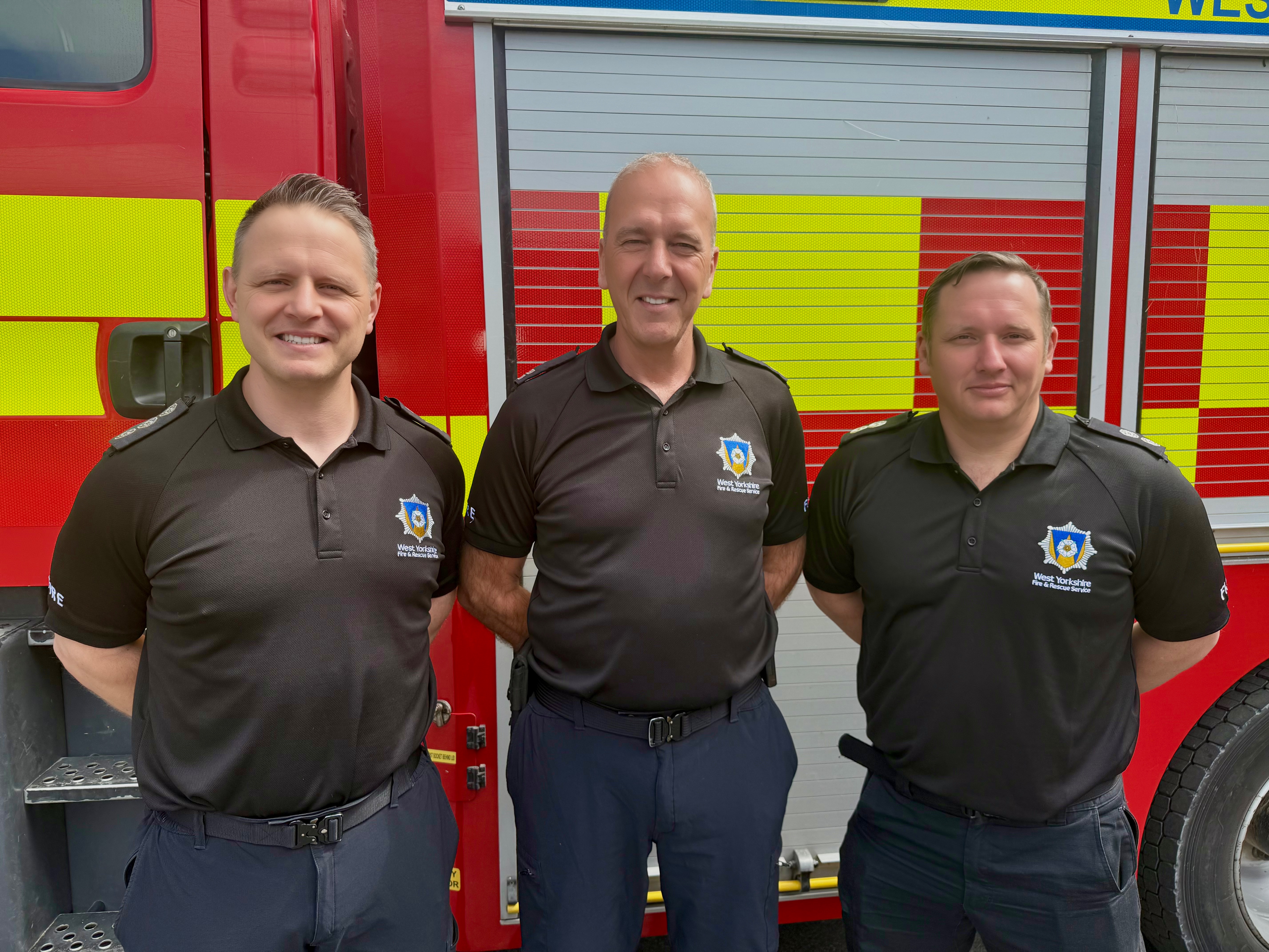 ADC Wolski, CM Warman and WM Shaw standing in front of a fire appliance in their black WYFRS uniform