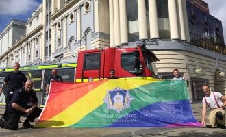 Staff holding up Fire Pride flag in front of Bradford theatre. 