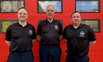 CM Warman standing in front of a fire appliance in their black WYFRS uniform