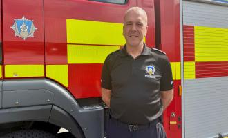 CM Warman standing in front of a fire appliance in their black WYFRS uniform
