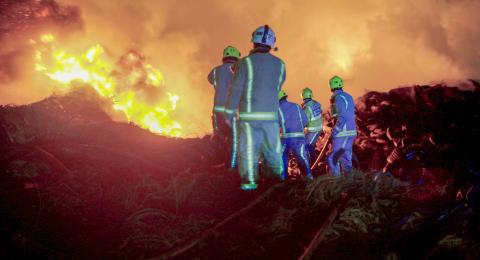 Firefighters standing in front of large fire.