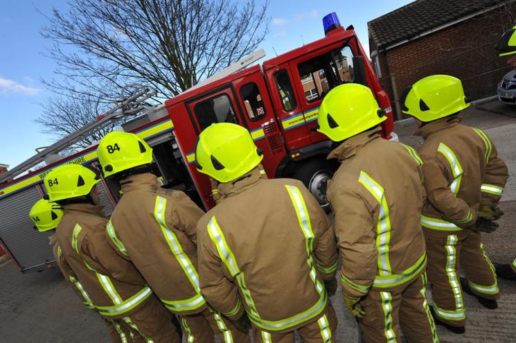 Firefighters stood together in front of fire engine. 