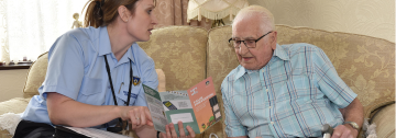 Member of protection staff sat with elderly gentleman looking at safe and well leaflet.