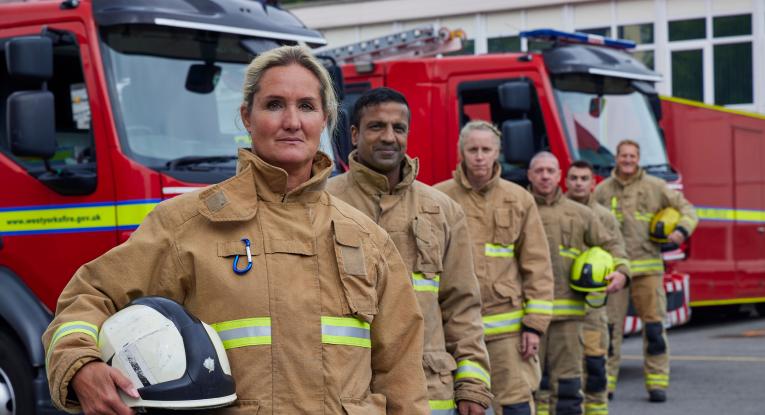 Firefighters stood in front of fire engines, looking at the camera. 