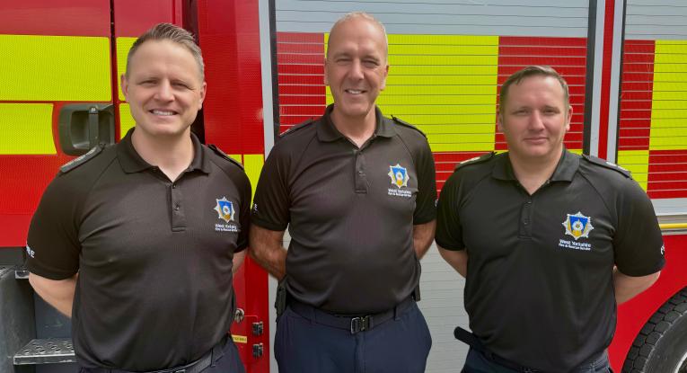ADC Wolski, CM Warman and WM Shaw standing in front of a fire appliance in their black WYFRS uniform
